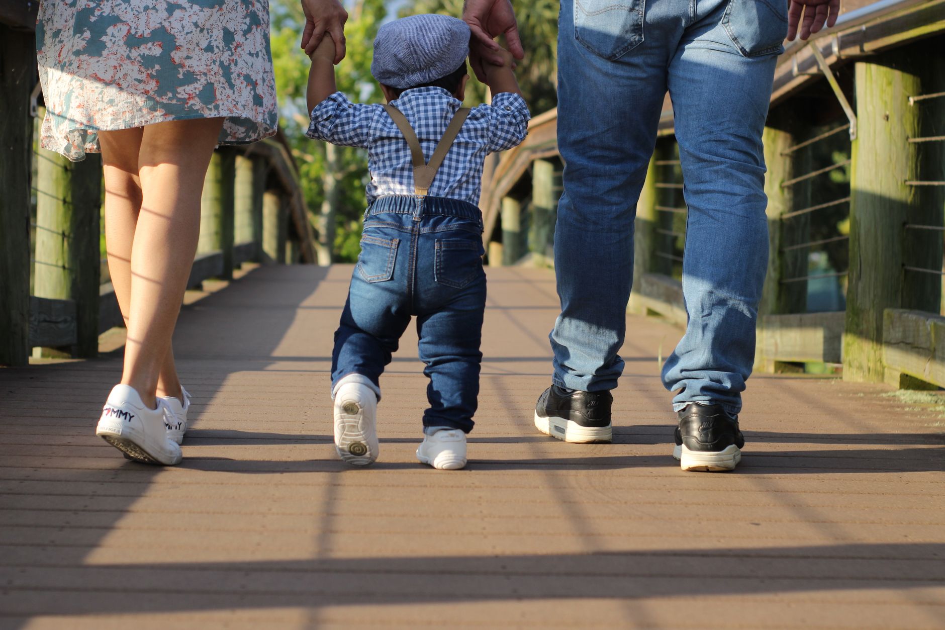 Ouders lopen hand in hand met hun kind over een vlonderpad, op de rug gezien